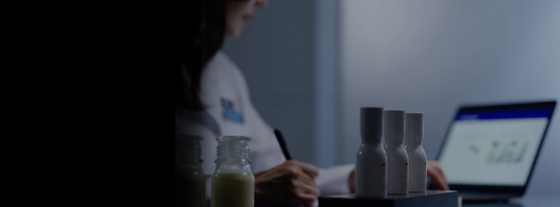 Person sitting at a desk with bottles and a laptop in a dimly lit room